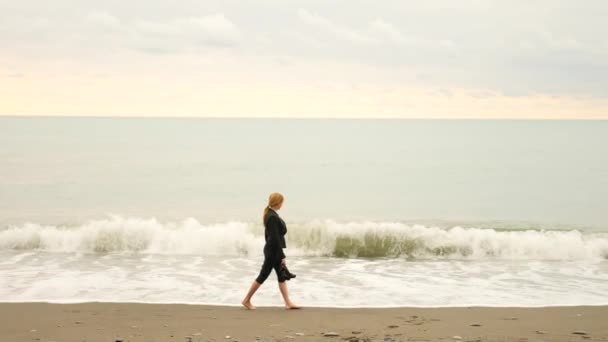 Donna d'affari in giacca e cravatta in piedi sulla spiaggia. si gode la vista sul mare. 4k, rallenta. piedi in onde da vicino — Video Stock