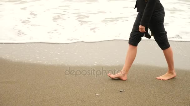 Donna d'affari in giacca e cravatta in piedi sulla spiaggia. si gode la vista sul mare. 4k, rallenta. piedi in onde da vicino — Video Stock