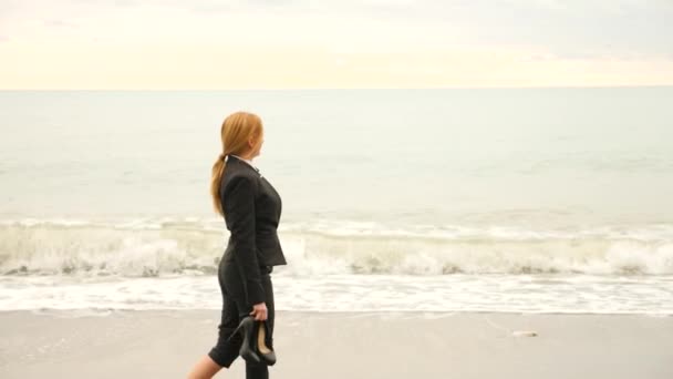 Zakenvrouw in pak staande op strand. Ze geniet van het uitzicht op zee. 4k, slow-motion. voeten in golven close-up — Stockvideo