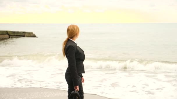 Mulher de negócios de terno em pé na praia. Ela gosta da vista para o mar. 4K, câmara lenta. pés em ondas fechar — Vídeo de Stock