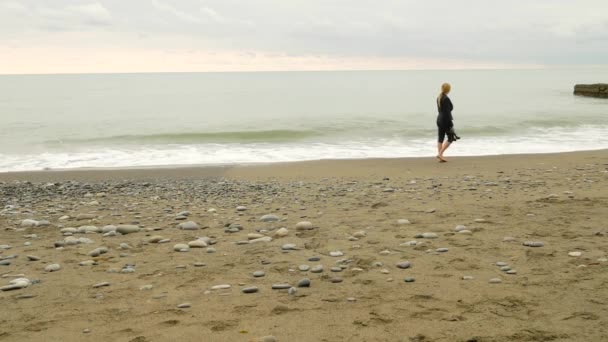 Interesu w garniturze stojącego na plaży. ona cieszy się widokiem na morze. 4k, zwolnionym tempie. stopy w fale z bliska — Wideo stockowe