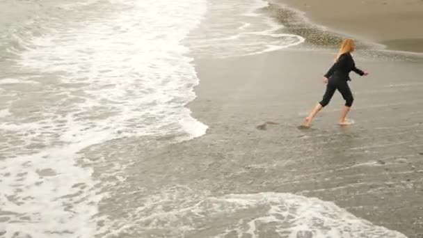 Mulher de negócios de terno em pé na praia. Ela gosta da vista para o mar. 4K, câmara lenta. ela tira o casaco — Vídeo de Stock