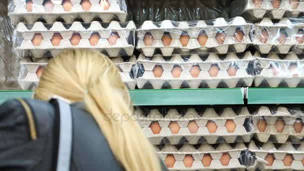 Jovem faz compras no supermercado, escolhe ovos. 4k, tiro em câmera lenta, espaço de cópia — Vídeo de Stock