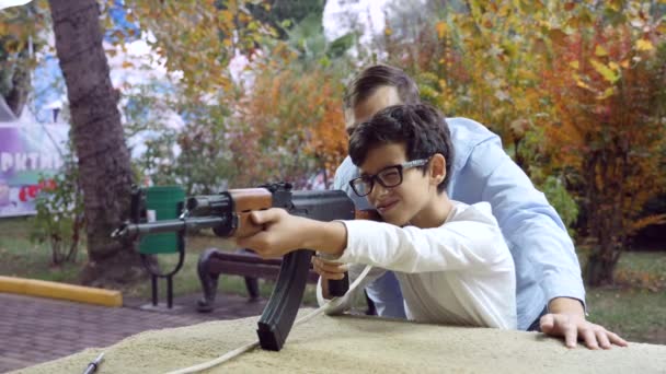 Joven dispara en un tablero de juego de un rifle de asalto Kalashnikov, 4k, airsoft. familia, entretenimiento en un parque de diversiones. Papá y su hijo están disparando a un guion . — Vídeos de Stock