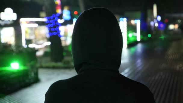 Силует чоловіка в капюшоні, що стоїть на нічній вулиці. 4k — стокове відео