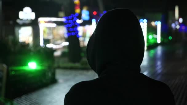 Silhouet van een man in een capuchon staande op een straat van de nacht. 4k — Stockvideo