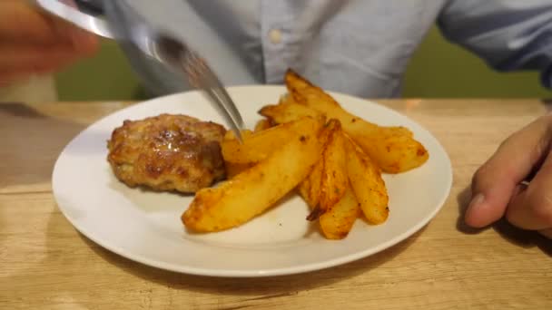 O homem está comendo costeletas de carne frita com batata assada em especiarias. 4k . — Vídeo de Stock