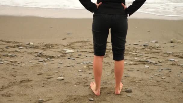 Femme d'affaires en costume debout sur la plage. elle aime la vue sur la mer. 4k, au ralenti. pieds en vagues gros plan — Video