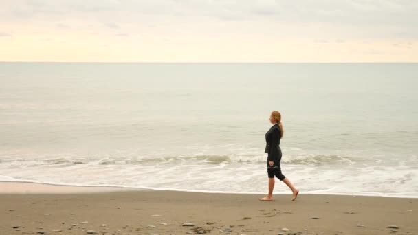 Üzletasszony strandján öltöny állandó. imádja a tengerre. 4k, lassú mozgás. láb hullámok közelről — Stock videók