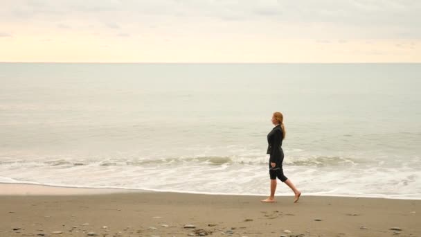 Geschäftsfrau im Anzug steht am Strand. Sie genießt den Meerblick. 4k, Zeitlupe. Füße in Wellen aus nächster Nähe — Stockvideo