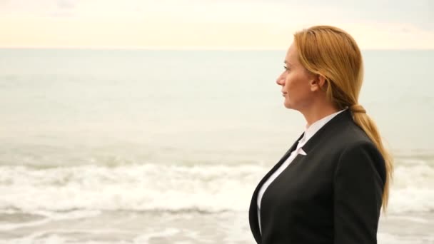 Businesswoman in suit standing on beach. she enjoys the sea view. 4k, slow motion. feet in waves close up — Stock Video