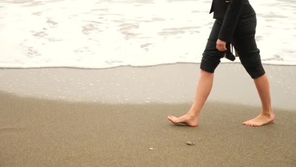 Femme d'affaires en costume debout sur la plage. elle aime la vue sur la mer. 4k, au ralenti. pieds en vagues gros plan — Video