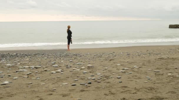 Mujer de negocios en traje de pie en la playa. disfruta de la vista al mar. 4k, cámara lenta. pies en olas de cerca — Vídeo de stock
