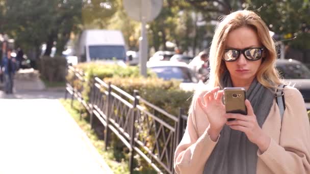 Mujer joven usando un teléfono inteligente, de pie en una zona comercial de la ciudad, 4k. Movimiento lento — Vídeos de Stock