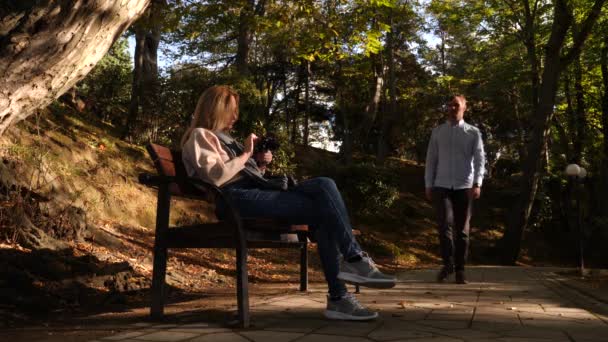 4k, au ralenti, fille avec une caméra est assis sur un banc dans un endroit pittoresque. Les passants passent devant . — Video