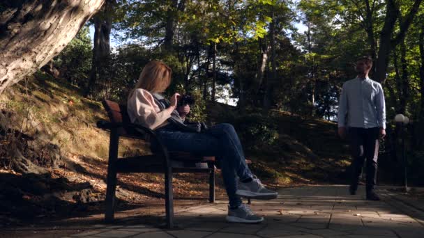 4k, rallentatore, ragazza con una macchina fotografica si siede su una panchina in un posto pittoresco. Passano i passanti . — Video Stock