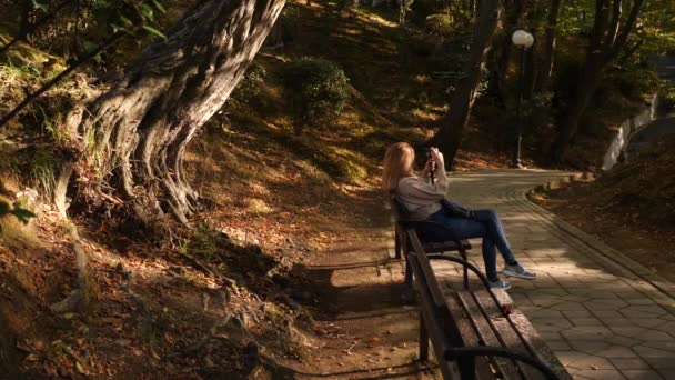 4k, slow-motion, girl with a camera sits on a bench in a picturesque place. — Stock Video