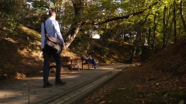 4k, slow-motion, girl with a camera sits on a bench in a picturesque place. Passers pass by. — Stock Video