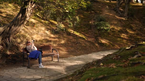 4k, slow-motion, girl with a camera sits on a bench in a picturesque place. — Stock Video