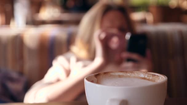 4k, lassú mozgás. a szőke lány várja a kávézóban. és nézni a smartphone — Stock videók