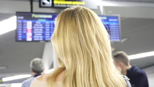 Una mujer mira el tablero de información en la sala de espera en el aeropuerto. Esperando el vuelo en el aeropuerto. 4k, cámara lenta — Vídeo de stock