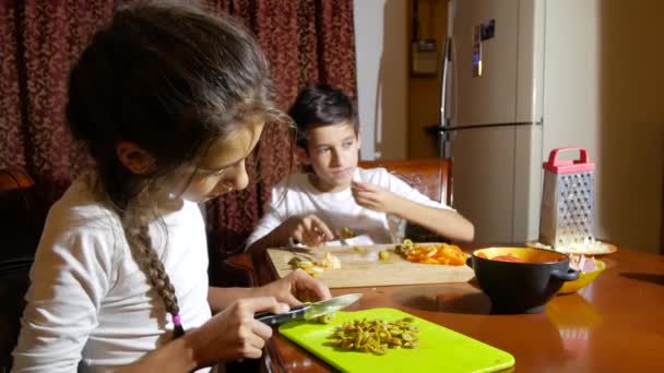 Bruder und Schwester schneiden eine Füllung für Pizza. Während die Familie Pizza kocht, kocht sie in der Küche. 4k — Stockvideo