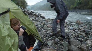 bir turist çadır 4 k. görünümünden bir dağ nehir üzerinde. Kız adamla çay termosu şişe içine dökülen ve dağ nehir görünüyor.