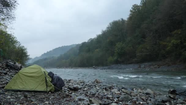 4k. ein Mann in der Nähe eines Touristenzeltes am Ufer eines Gebirgsflusses. — Stockvideo