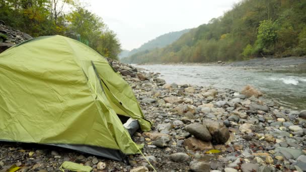 4k. un ragazzo vicino a una tenda turistica sulla riva di un fiume di montagna . — Video Stock