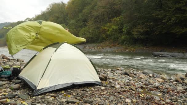 4k. il tipo mette una tenda turistica sulla riva di un fiume di montagna . — Video Stock