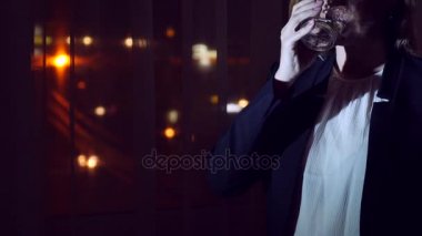 İçecek ayakta pencere tarafından evde gece içme iş elbiseli genç kadın. Panorama pencere, görünüm şehrin gece ışıkları. 4k