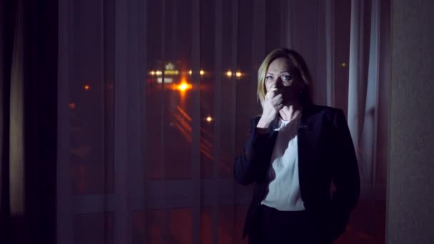Femme en costume d'affaires mangeant une pomme debout près de la fenêtre panoramique de nuit. vue sur la ville, veilleuses. 4k — Video