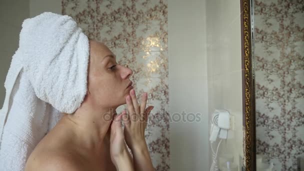 Kvinna som tillämpar mask fuktgivare för hud på ansikte titta i spegeln i badrummet. 4k, Slowmotion — Stockvideo