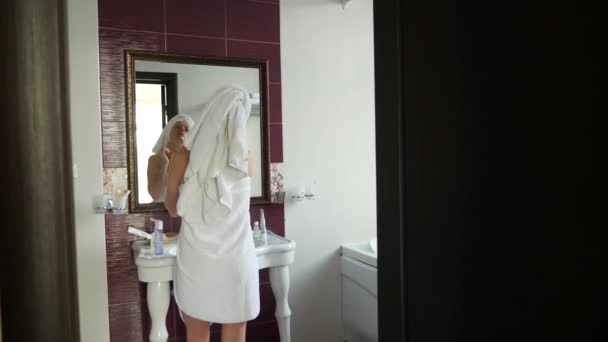 Donna che applica crema idratante maschera per la pelle sul viso guardando nello specchio in bagno. 4k, rallentatore — Video Stock