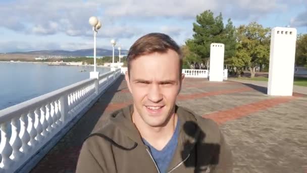Блог, технологии. счастливый улыбающийся человек или блогер с камерой, записывающей видео во время пробежки по набережной, 4K, замедленная съемка — стоковое видео