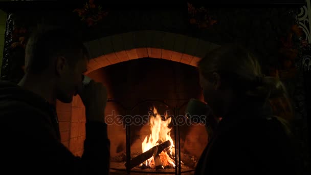 Fuego en una chimenea. 4k, cámara lenta. hombre y mujer beben té cerca de la chimenea — Vídeo de stock