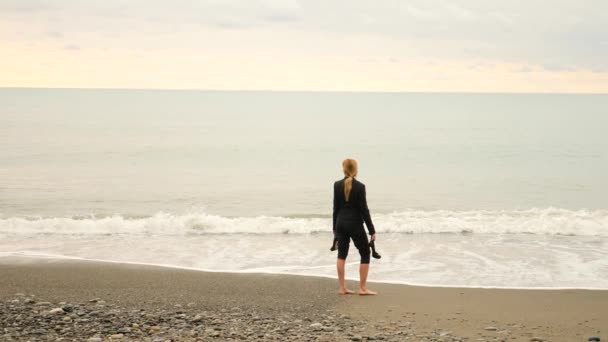 Mulher de negócios de terno em pé na praia. Ela gosta da vista para o mar. 4K, câmara lenta. pés em ondas fechar — Vídeo de Stock
