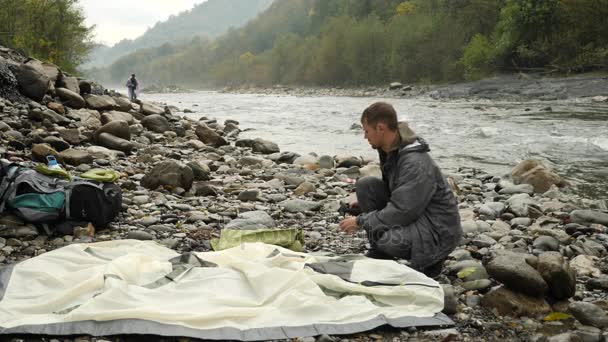 4k. le gars met une tente touristique sur le rivage d'une rivière de montagne . — Video
