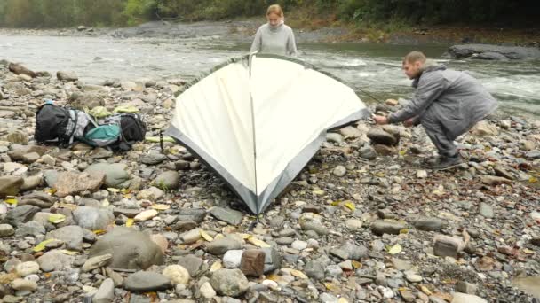 4 k. en kille och en tjej sätter en turist tält på stranden av en mountain river. Slow motion — Stockvideo