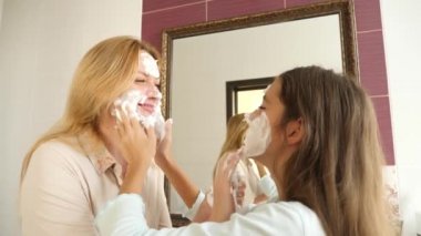 Annem ve onun kızı genç sabah banyoda yıka. köpük yıkama ile yüzlerini smear. 4k, ağır çekim