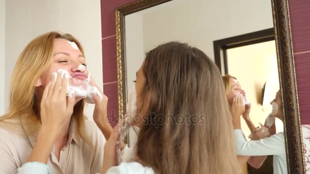 Moeder en haar dochter tiener wassen in de badkamer in de ochtend. zij smeren hun gezicht met schuim voor het wassen. 4k, slow-motion — Stockvideo
