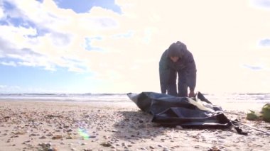 Denizin kenarında plajda kamp çadır. 4k, ağır çekim. bir adam bir çadır rüzgarlı havalarda kumlu bir plaj üzerinde kurar