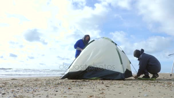 海のビーチでキャンプのテント。4 k、スローモーション。男と女は、砂浜でテント風の天気予報を設定します。 — ストック動画