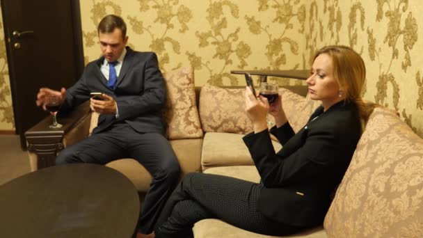 Dois homens de negócios, um homem e uma mulher de fato de negócios estão a beber vinho nas suites, sentados no sofá. 4k — Vídeo de Stock