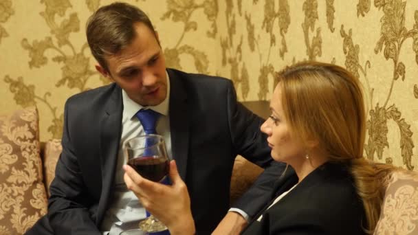 Ein paar Geschäftsleute, ein Mann und eine Frau in Business-Anzügen sitzen auf der Couch und trinken Wein in den Suiten. 4k — Stockvideo