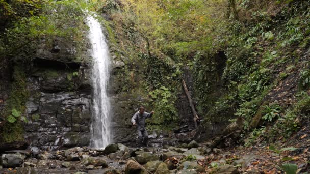 Felice uomo backpacker godendo incredibile cascata tropicale.Viaggio Stile di vita e concetto di successo vacanze nella natura selvaggia su sfondo montagna. 4k, rallentatore — Video Stock