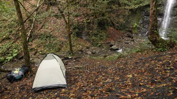 4k, lassú mozgás. férfi turisztikai sátorhelyek is sátor a lábánál a hegy melletti vízesés. — Stock videók