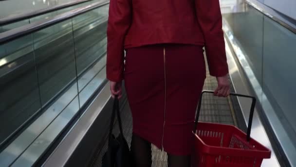 4k, cámara lenta, primer plano. una mujer en una escalera mecánica con una bolsa y una bolsa de compras para ir de compras. vista posterior — Vídeos de Stock