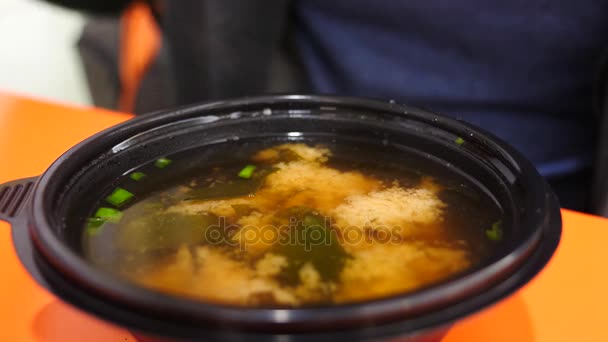 Ein Mann isst in einem Schnellrestaurant chinesisches Essen. 4k. Zeitlupe. Er isst Suppe aus einem Einwegteller — Stockvideo