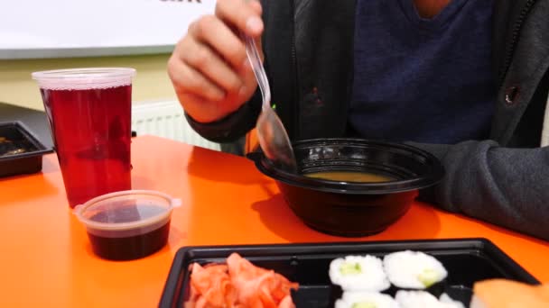 En man är att äta kinesisk mat i en snabbmatsrestaurang. 4 k. slowmotion. Han äter soppa från en disponibel tallrik — Stockvideo